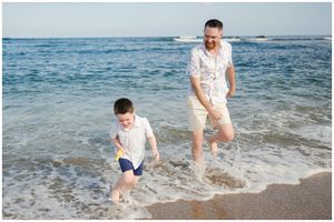 Two people wearing white and navy outfits run and splash together in the ocean waves at a sunny beach.
