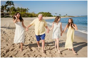 A group walking hand in hand along a tropical beach with palm trees and blue ocean water in the background.