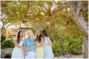 A group shares a candid moment outdoors under a large tree with golden autumn leaves and dappled sunlight.