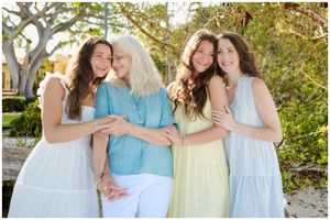 Group in pastel colored dresses and blue top sharing laughter together outdoors on sunny day.