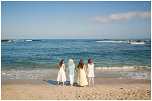Three figures in white dresses standing together at the ocean's edge on a sandy beach.