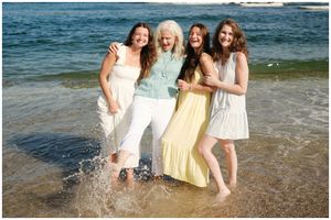 Friends enjoying a playful moment splashing in the ocean water at the beach wearing summer dresses and white pants.