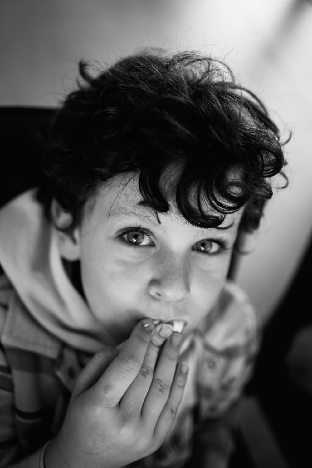 Black and white close-up portrait of a child biting their finger.