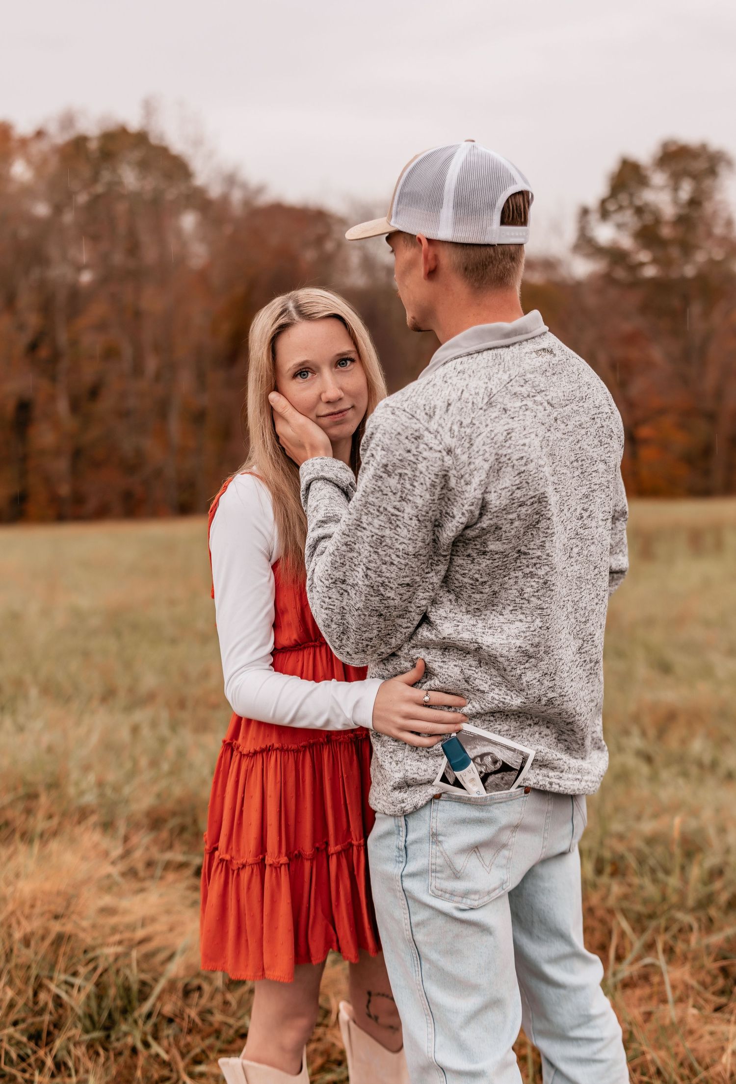 Couple sharing emotional moment in field during autumn pregnancy announcement.