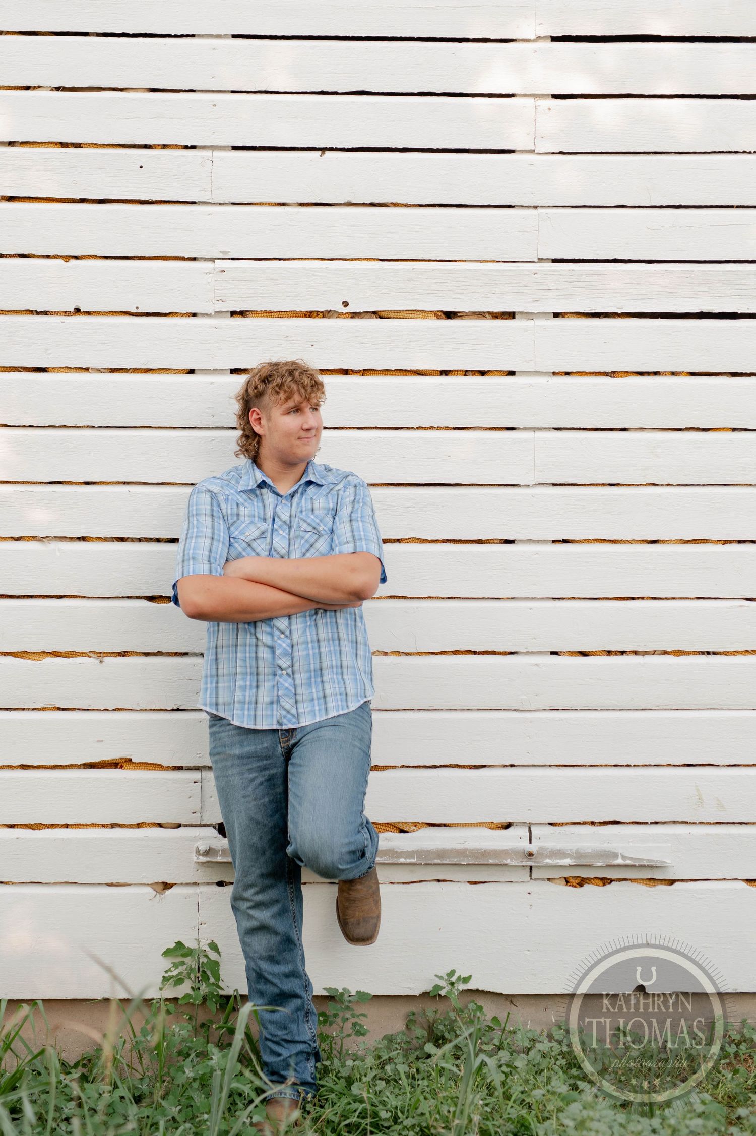 A casual portrait against weathered white barn siding with crossed arms and boots.
