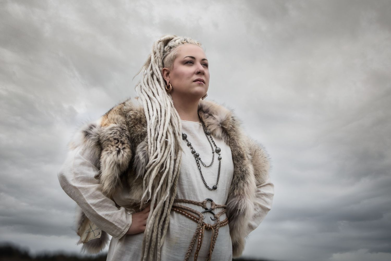 A dramatic portrait against stormy skies featuring someone in fur and white clothing.
