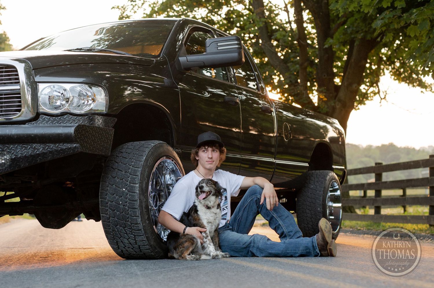Custom black Dodge Ram pickup truck with small dog beside it at golden hour.