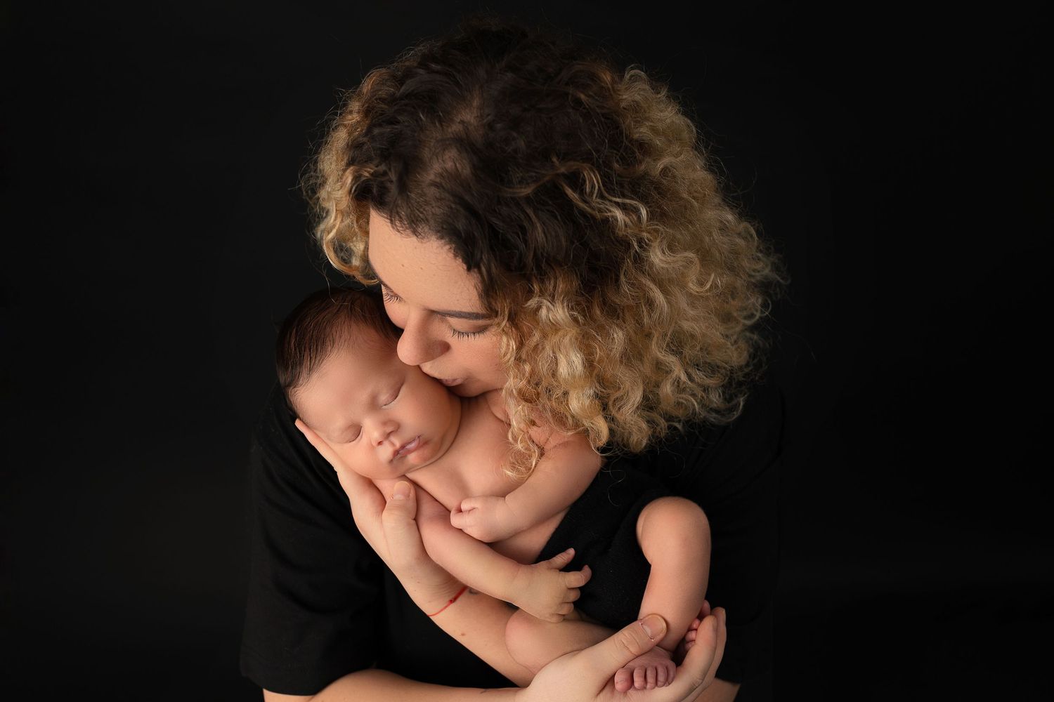 Tender newborn photography portrait on black backdrop showing parent gently cradling sleeping baby.