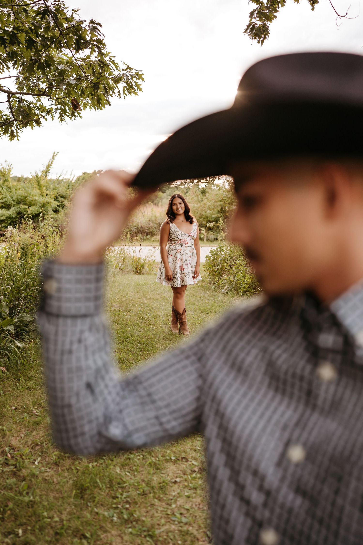 A couple poses in a grassy field on a sunny day with one person in the foreground wearing a plaid shirt.