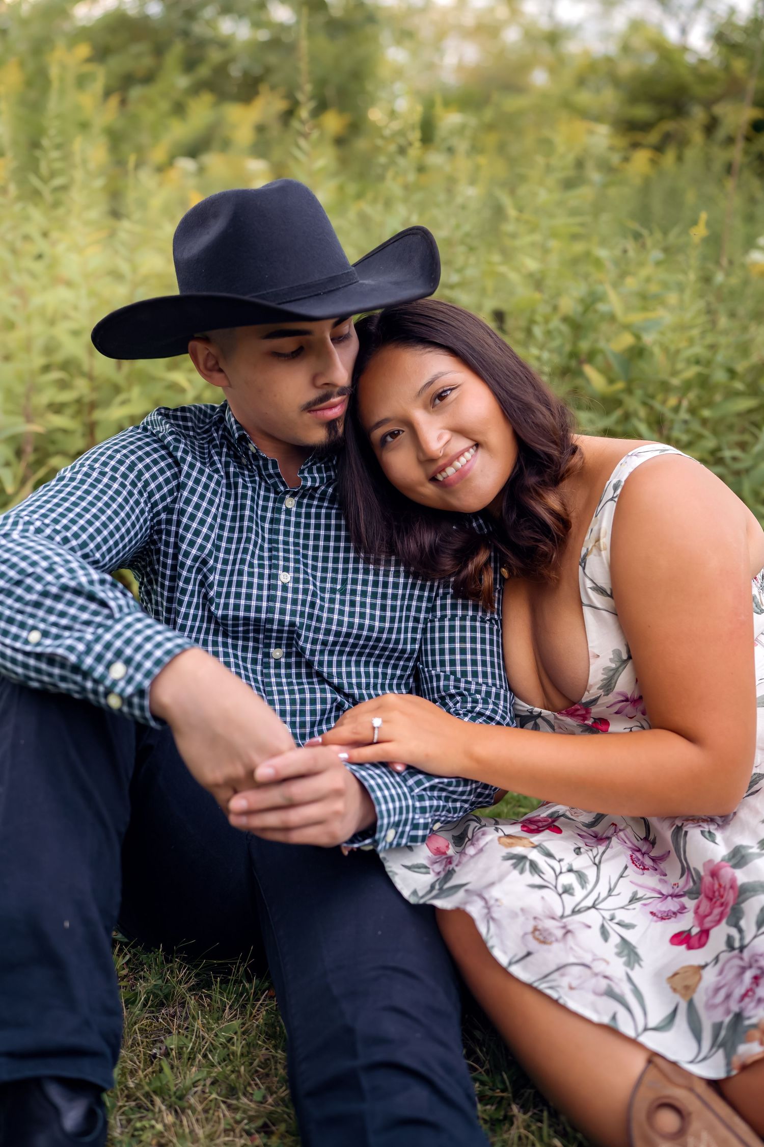 A romantic couple relaxes in a grassy field wearing coordinating outfits of plaid and floral prints.