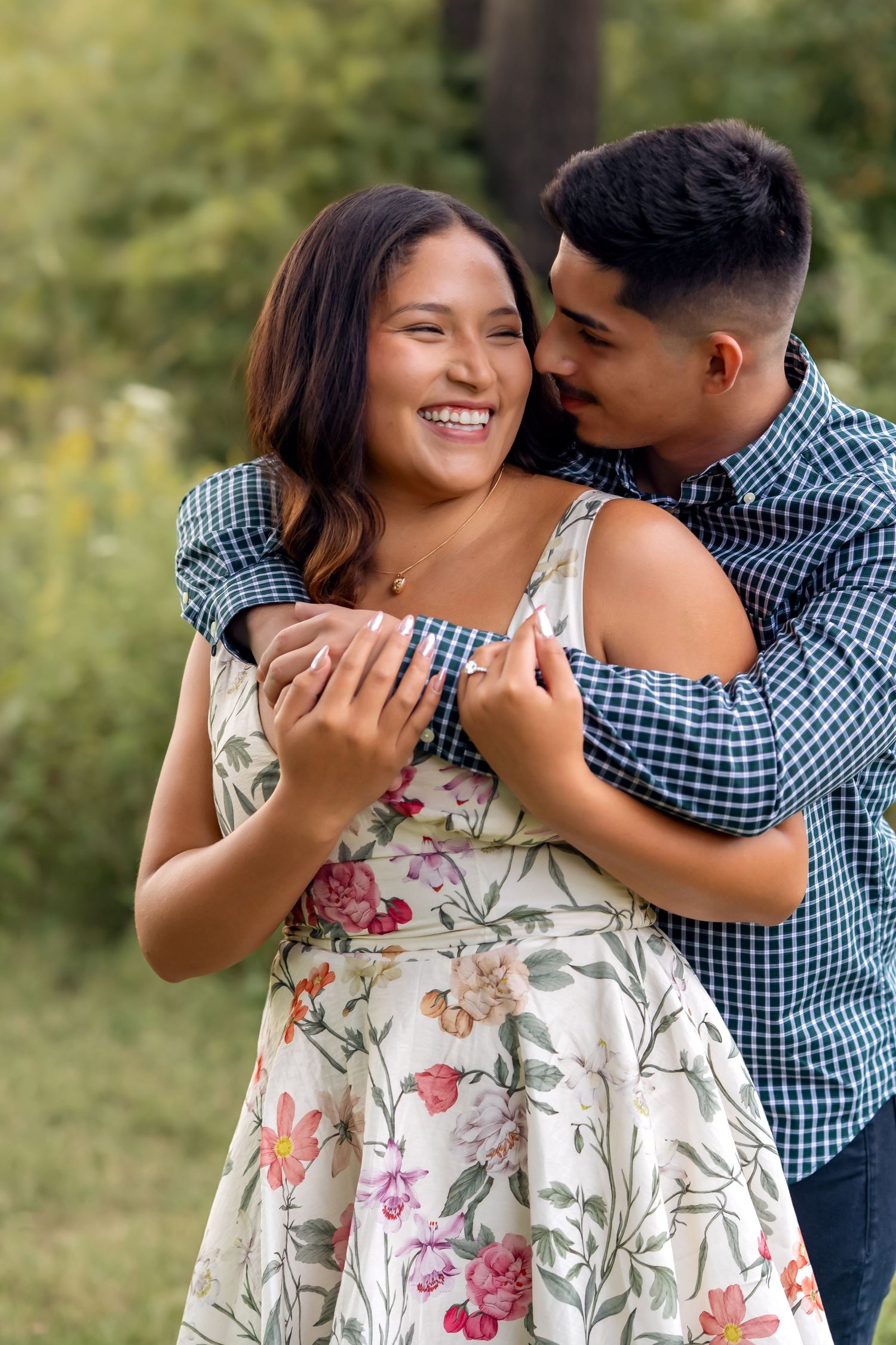 A couple shares laughter and embraces while posing for outdoor photos in casual attire.