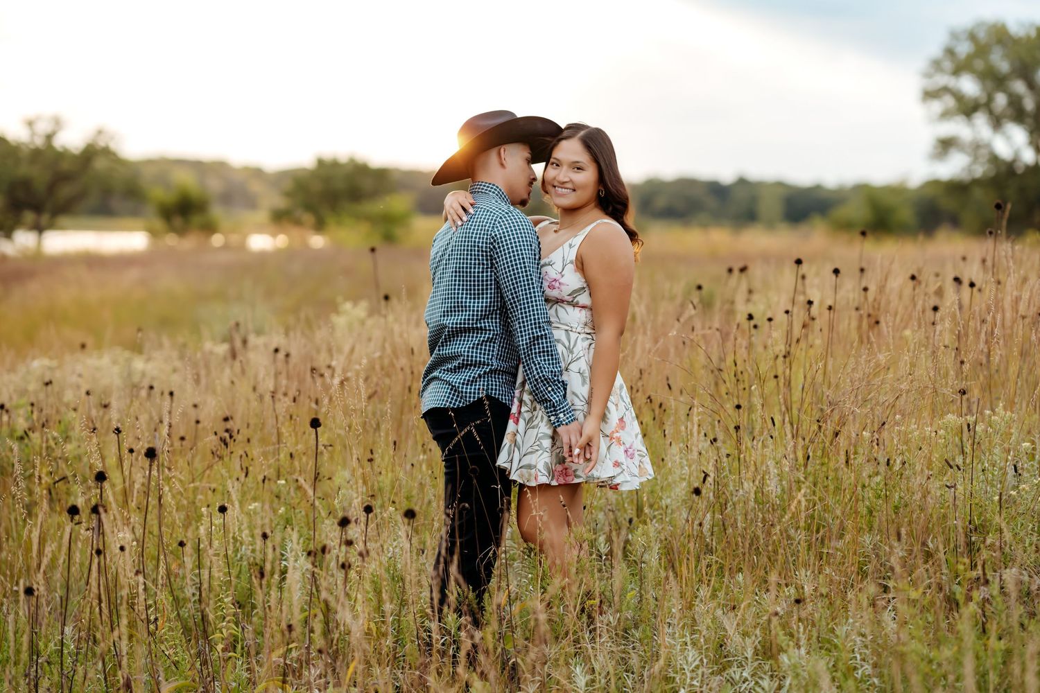 A couple embraces in a golden meadow during sunset as wildflowers sway in the gentle breeze.
