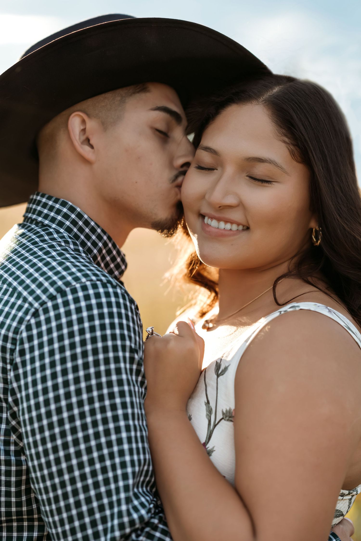 A romantic couple embraces during a golden hour photoshoot, with soft sunlight creating a warm, intimate atmosphere.
