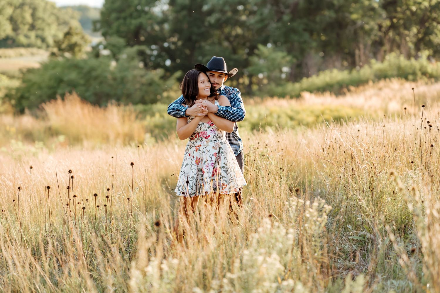 A couple shares a tender moment together in a golden sunlit meadow during a summer photo session.