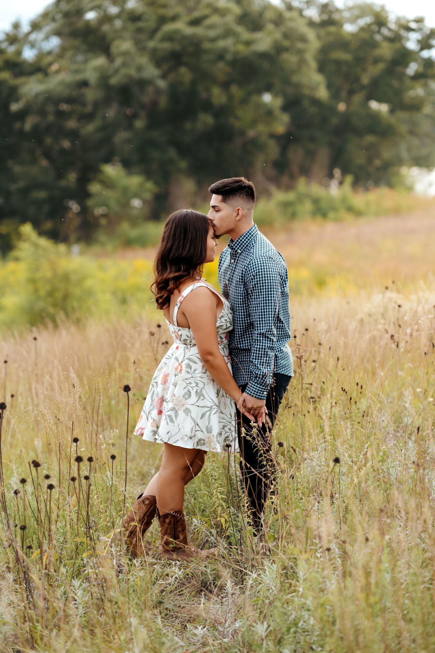A romantic couple shares tender moments in a sunlit meadow with tall grass and wildflowers during a summer photo session.