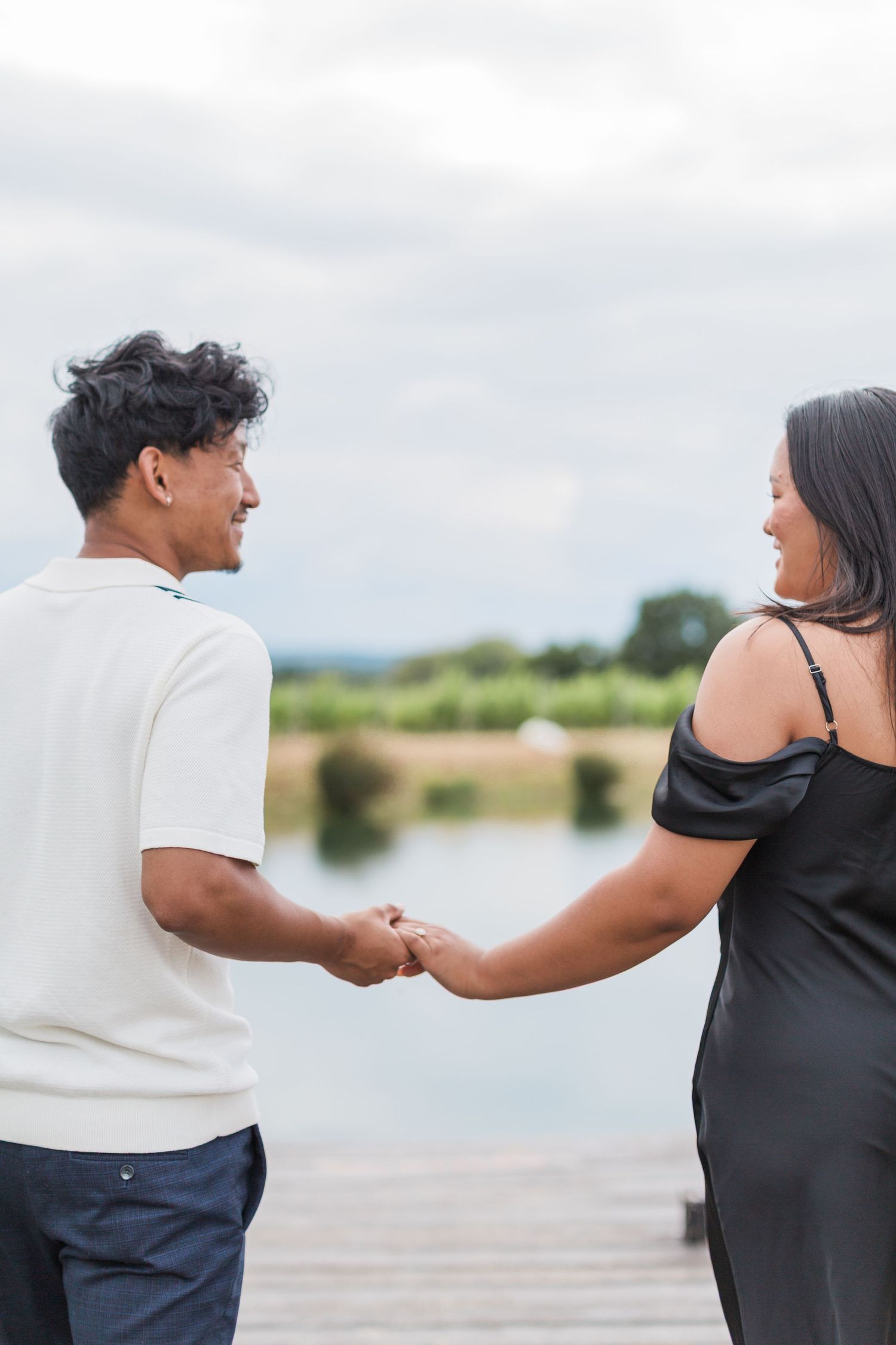 A newly engaged couple holding hands while standing on a wooden dock by a serene lake - proposal photography Hayley elizabeth