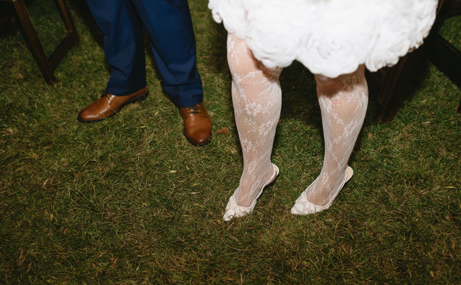 Wedding guests' feet and legs shown dancing and celebrating on grass at an outdoor reception.