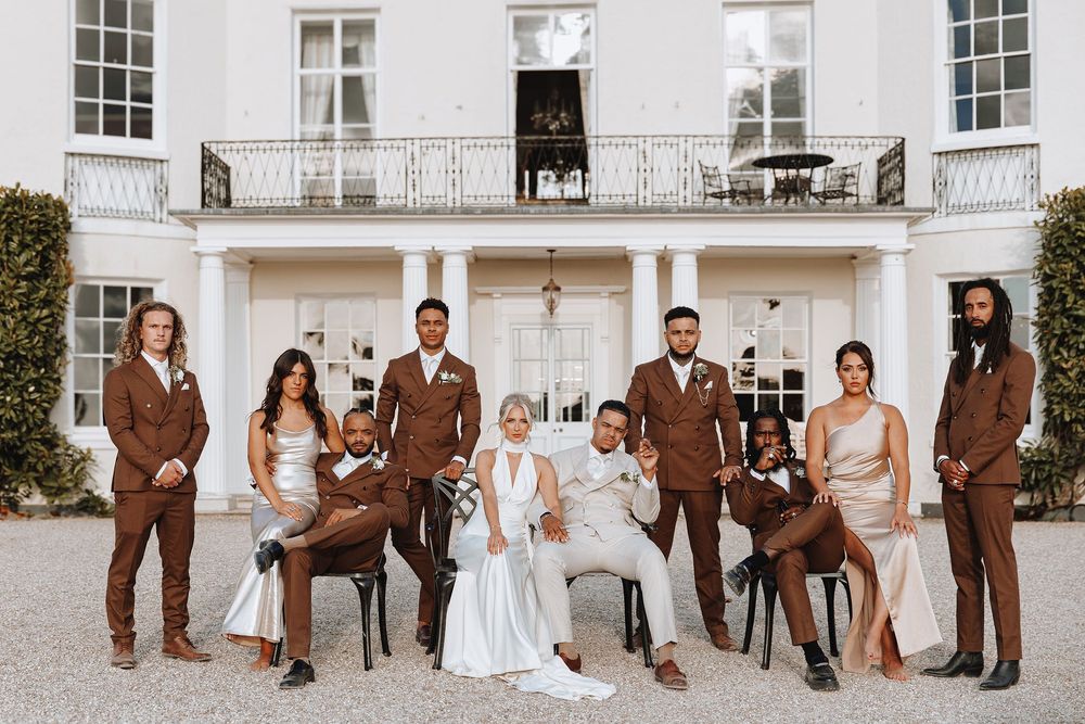Wedding party poses for formal group photos in front of elegant white building with columns and balconies.