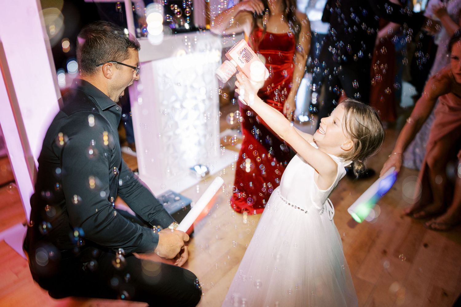 A couple dances together during their first dance at a wedding reception while red confetti falls around them.