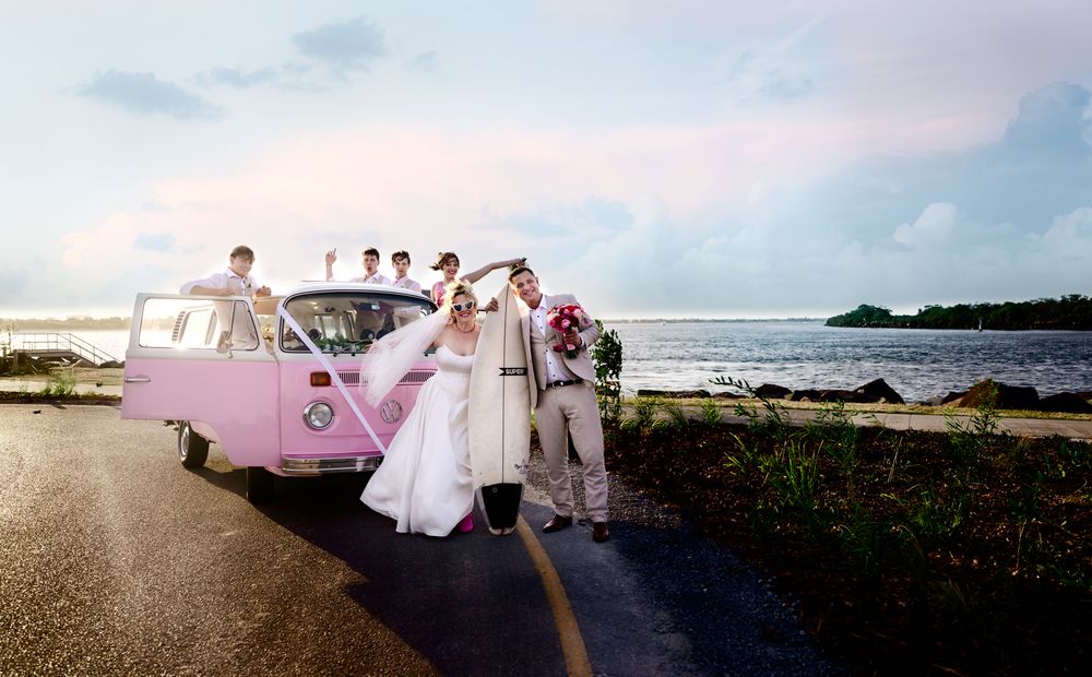 Wedding party holds flowing white dress fabric on a beach at sunset with ocean waves in the background.