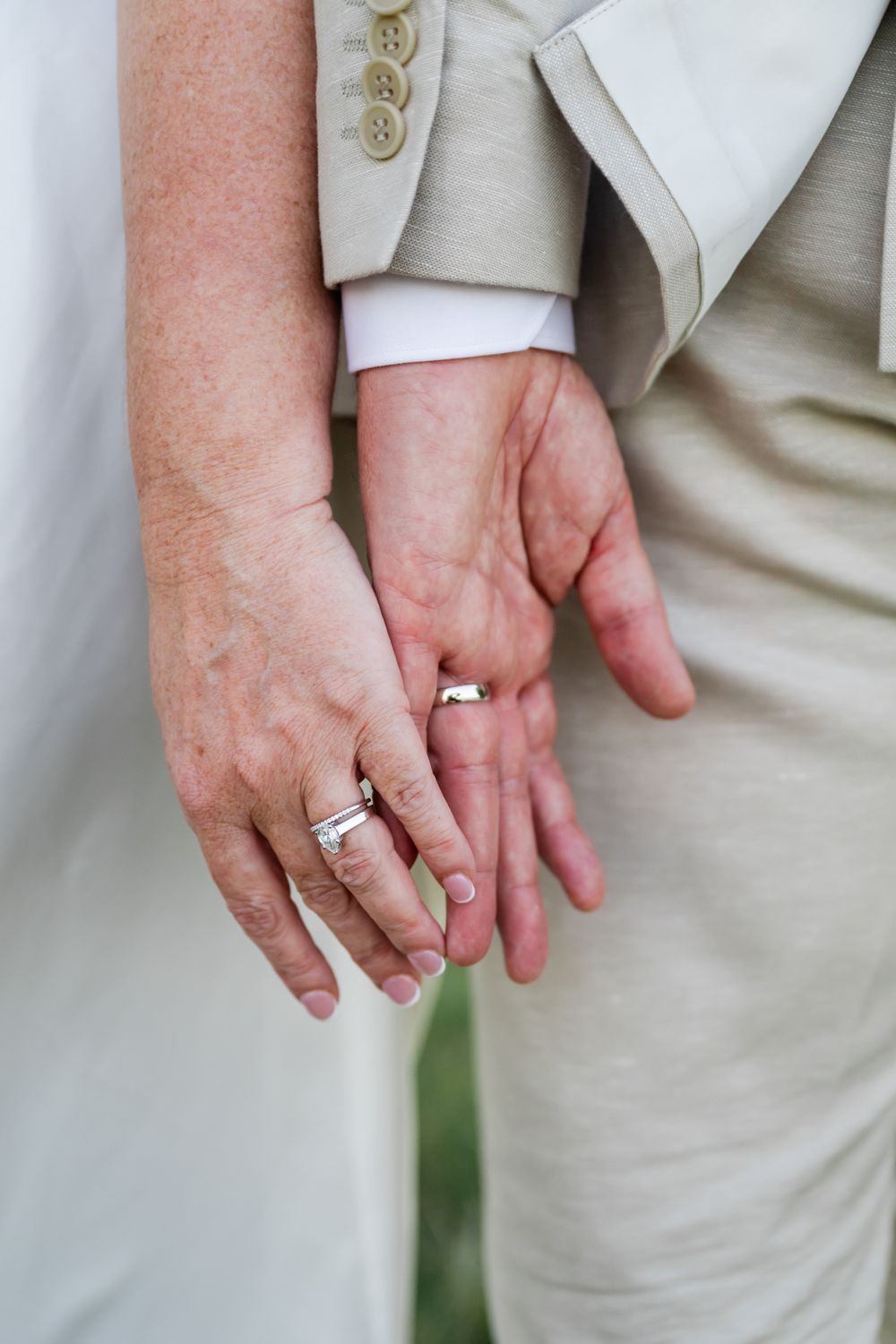 Close-up of hands displaying wedding rings against light-colored formal attire.