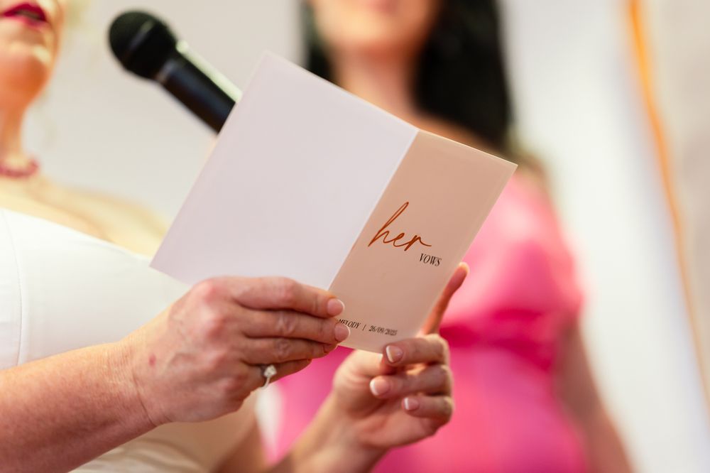 Bridesmaids in pink dresses read from small white cards during a wedding ceremony.