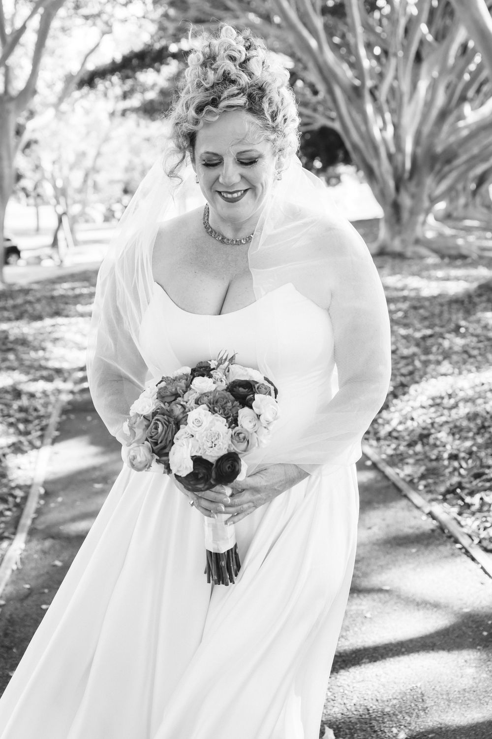 A bride in a white wedding dress holds a bouquet of pink and burgundy flowers in a garden setting.