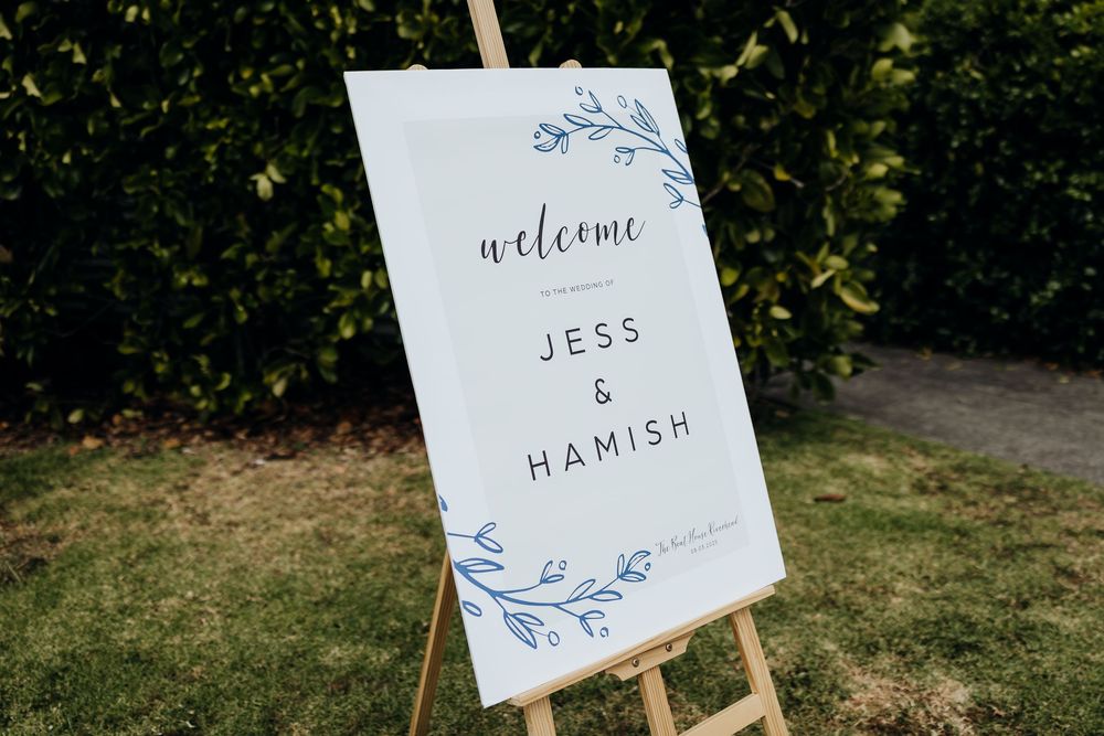 Elegant blue and white wedding welcome sign displayed on wooden easel outdoors.