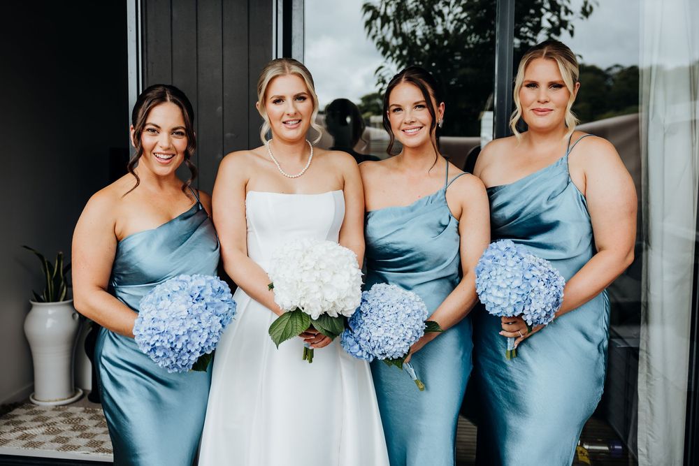 Bridal party wearing light blue satin dresses pose together with bouquets.