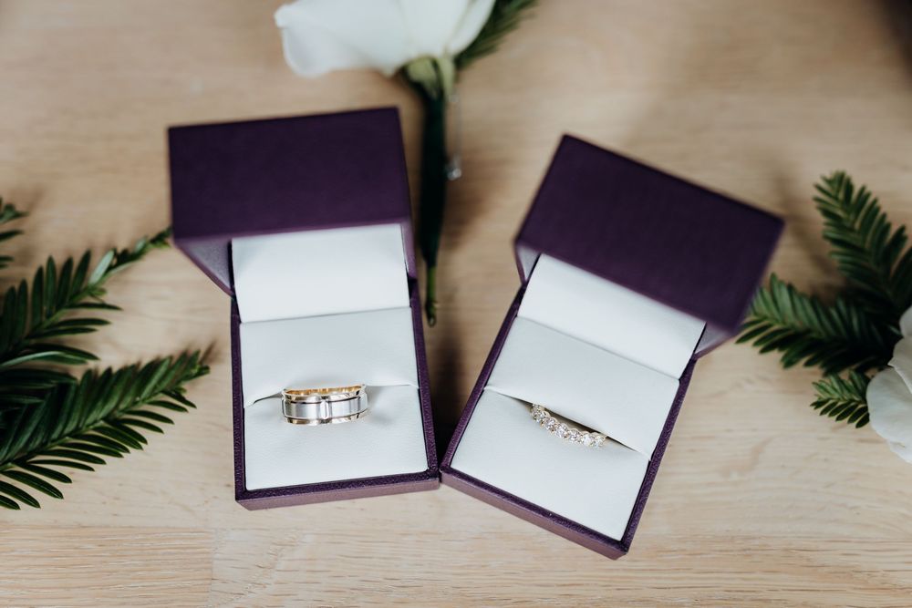 Purple wedding invitation boxes with greenery laid out on wooden surface.