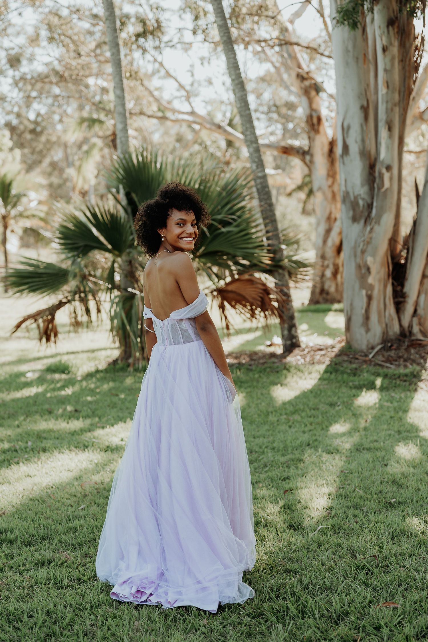 Person in flowing white dress twirling among eucalyptus trees in gladstone garden setting.