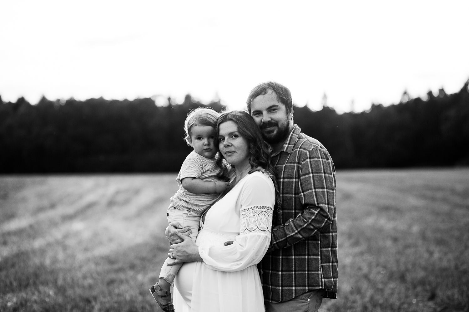 A series of black and white maternity photos showing a couple embracing in an outdoor field setting.
