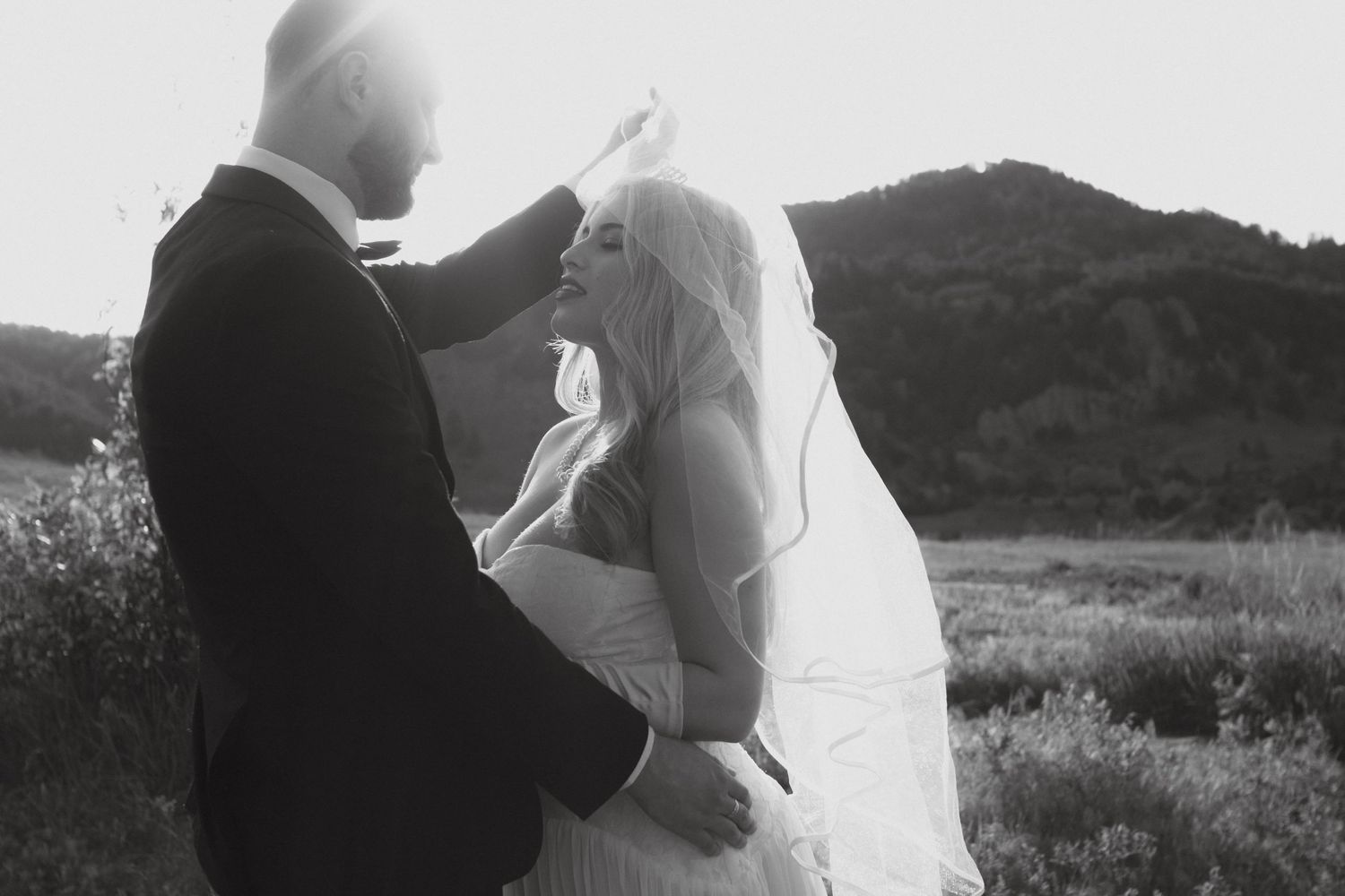 A couple in wedding attire embraces while dancing together in a scenic outdoor setting at sunset.