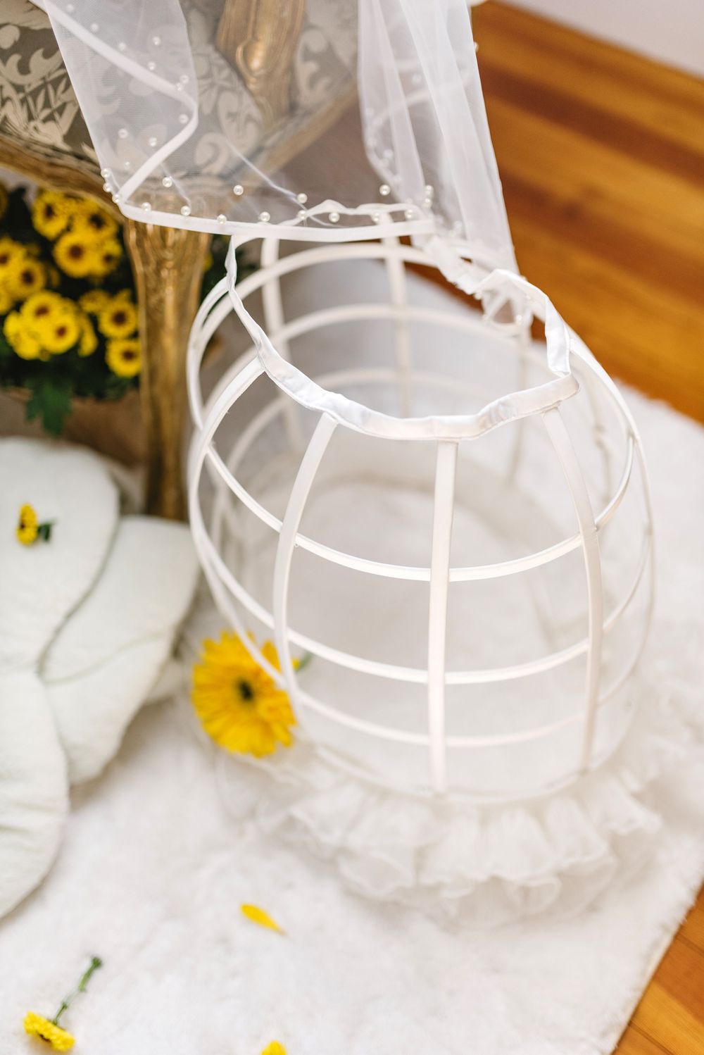 Close-up of white bridal crinoline and veil with yellow flowers on wooden floor.