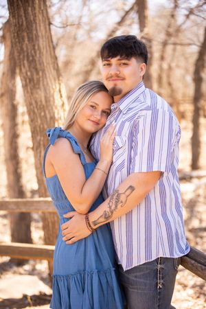 A romantic couple poses together against a tree in autumn woods, with soft golden lighting.