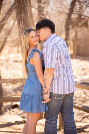 A couple in blue dress and striped shirt share intimate moments in a sunlit outdoor setting.