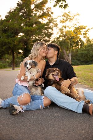 Couple relaxing outdoors on pavement at sunset with their Australian Shepherd dog in casual denim attire.