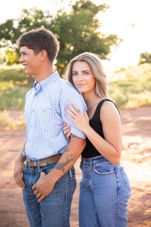 A couple embraces outdoors during a romantic sunset photoshoot in casual western attire.