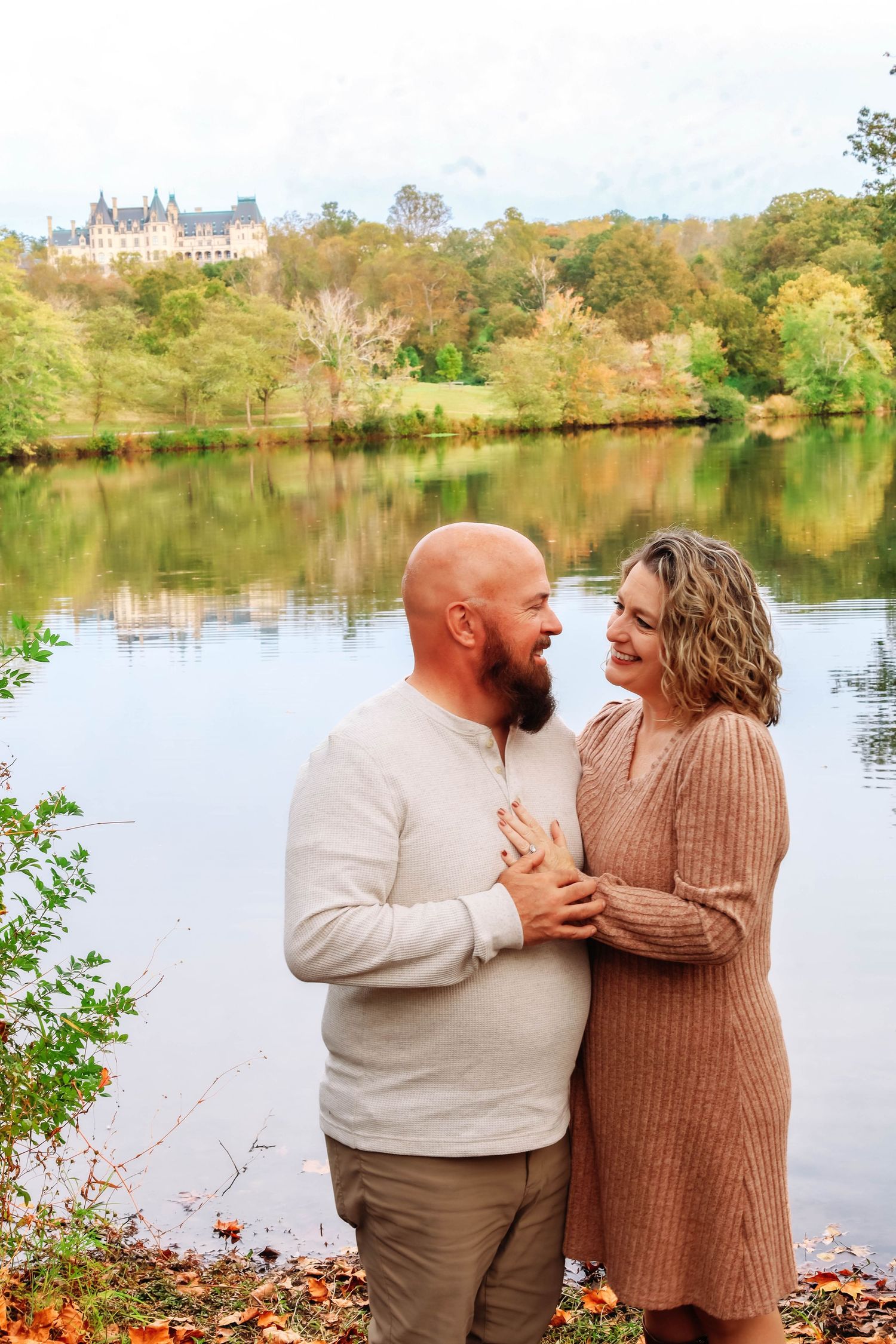 Couple in cozy sweaters sharing romantic moments by a scenic autumn lake with fall foliage in the background.