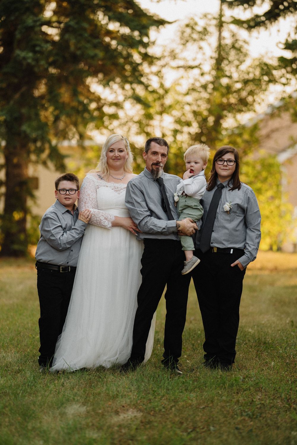 A wedding family portrait with bride, groom, and three children posing outdoors.