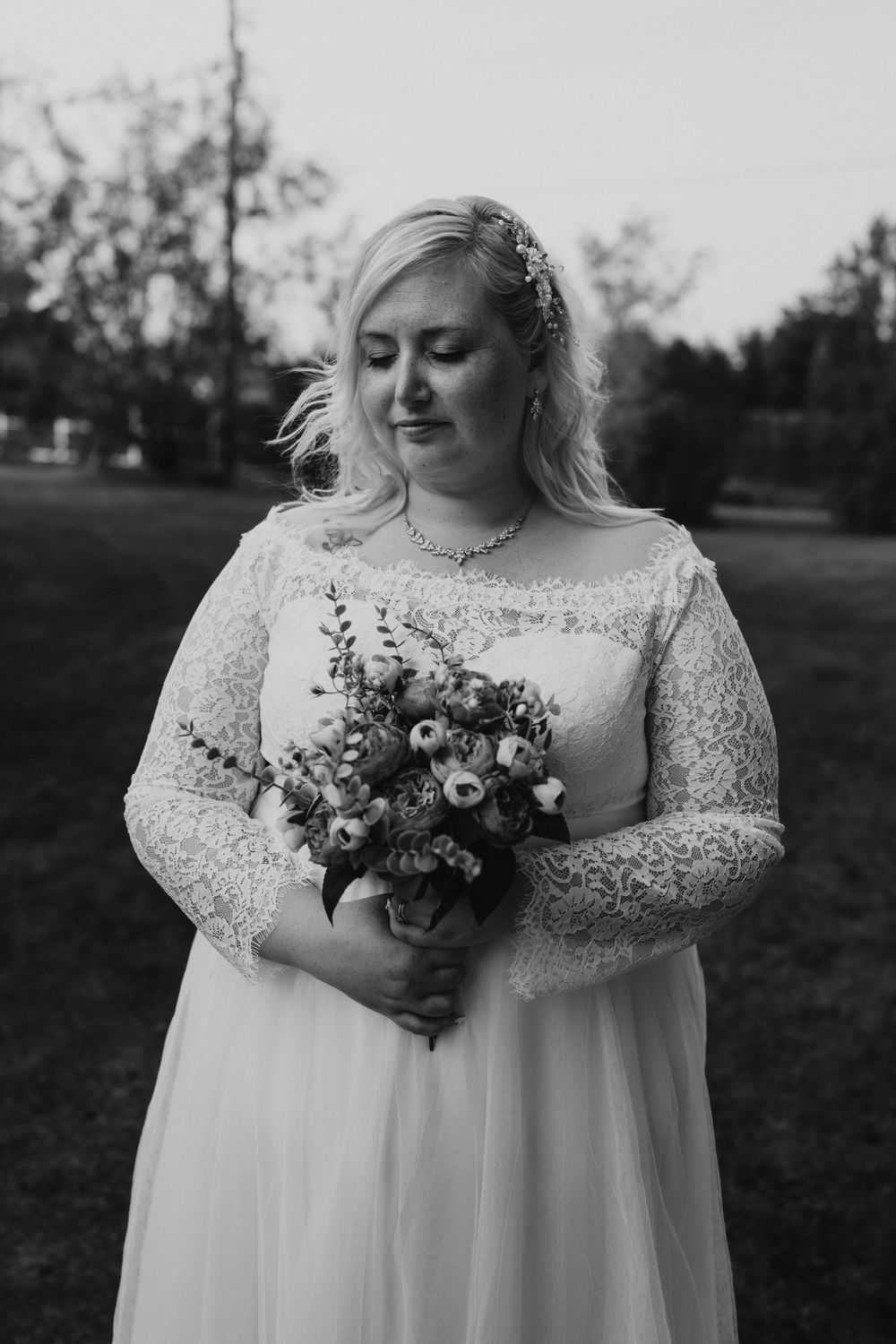 Black and white portrait of a bride in lace gown holding a wildflower bouquet outdoors.