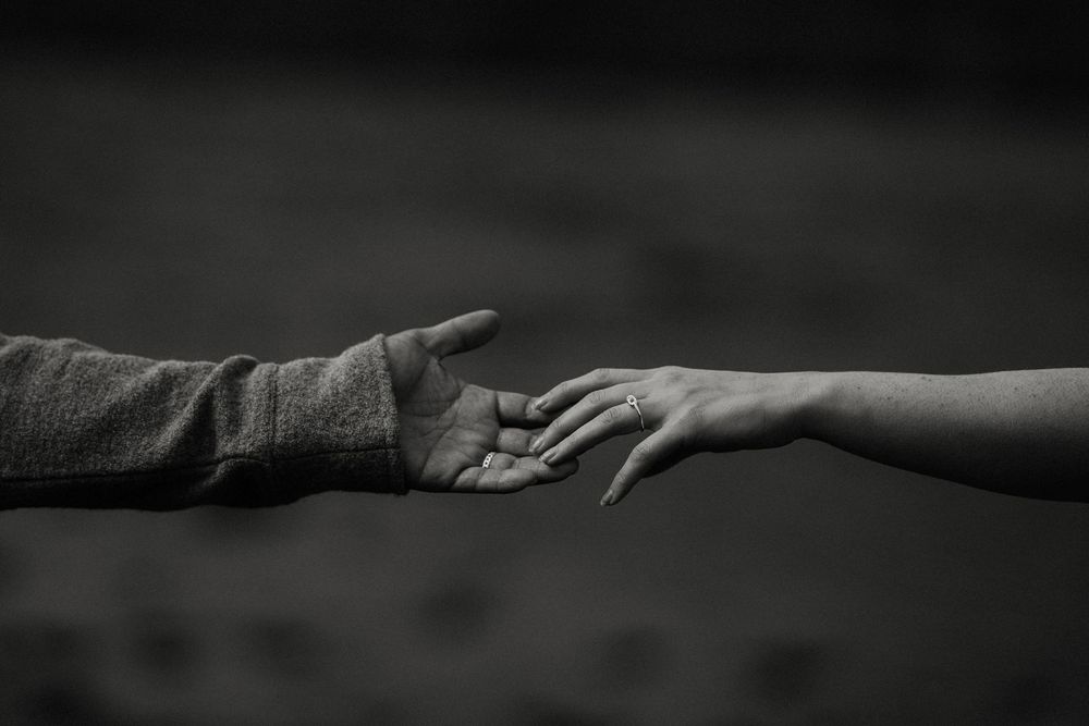 Black and white close-up of two hands reaching toward each other in a tender gesture.