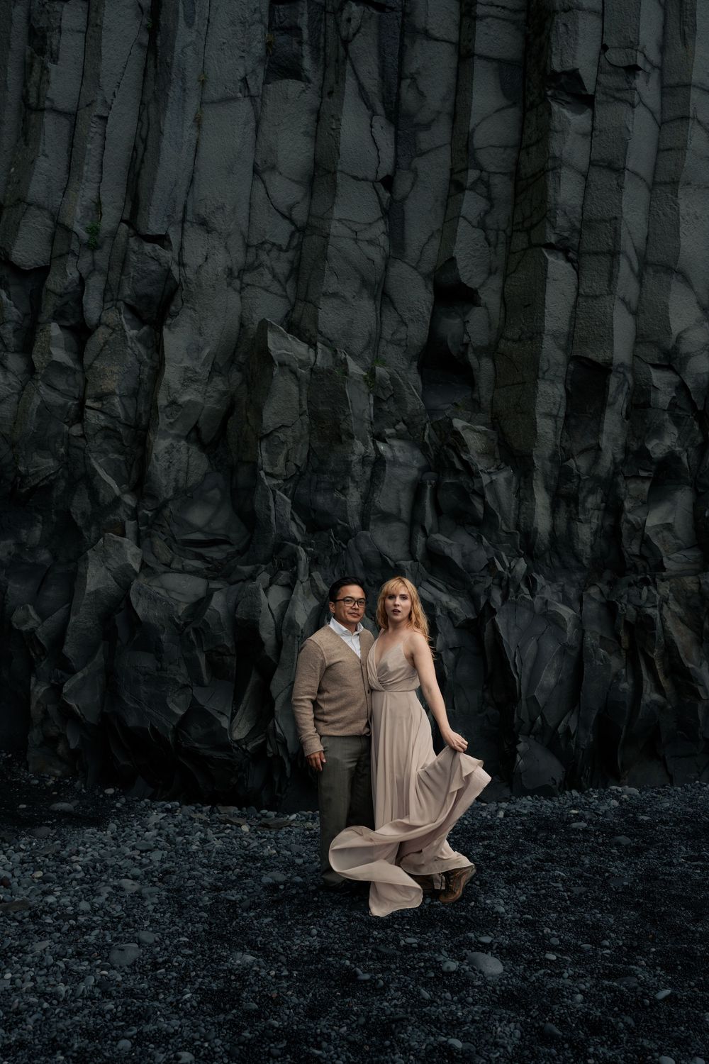 Couple posing against dramatic dark basalt rock columns on Iceland's black sand beach.
