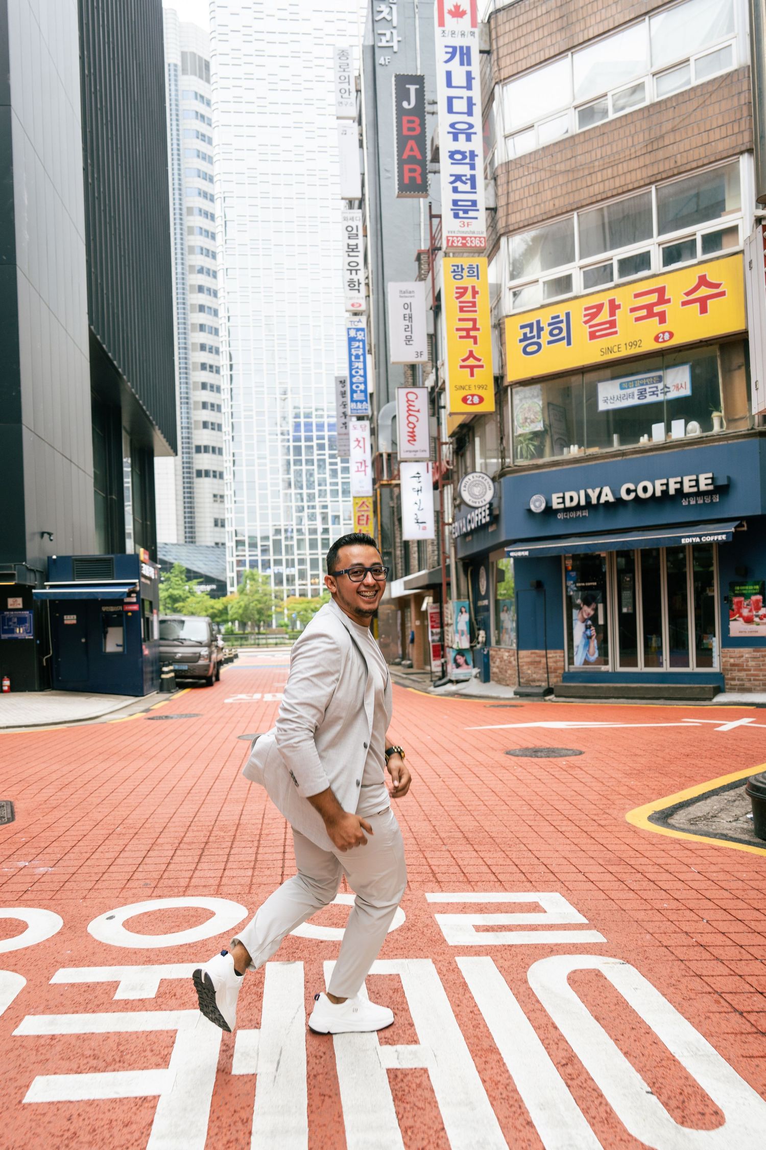 A person in white clothing performs dynamic poses on a red brick sidewalk in an urban Asian setting.
