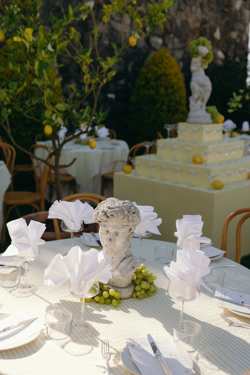 Elegant white table settings with decorative busts and green grapes arranged on a striped tablecloth for a formal event.