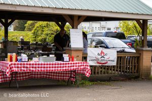 Long covered pavilion with red checkered tablecloths and vendor displays set up for an outdoor event.
