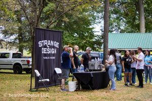 Outdoor festival setup with vendor booths and banners under trees on a sunny day.