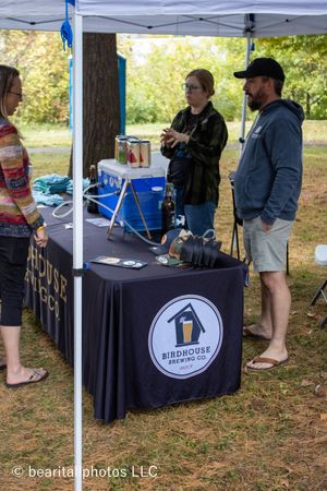 Vendor booth with black tablecloth and branded display under white tent at outdoor event.