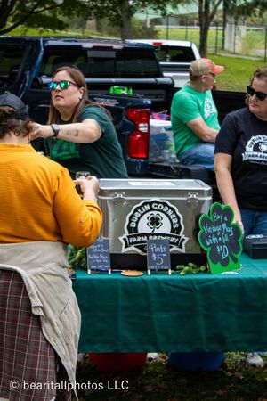 Vendor booth with green tablecloth displaying craft beer merchandise and signs.