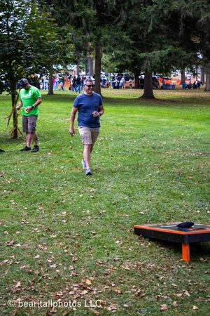 Grassy outdoor area with scattered fall leaves and cornhole boards set up for games.